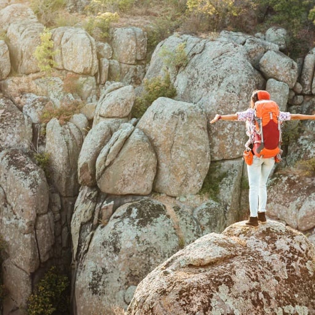Una persona posando sobre una roca en un acantilado con los brazos abiertos. Viaje de aventuras.