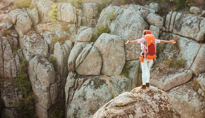 Una persona posando sobre una roca en un acantilado con los brazos abiertos. Viaje de aventuras.