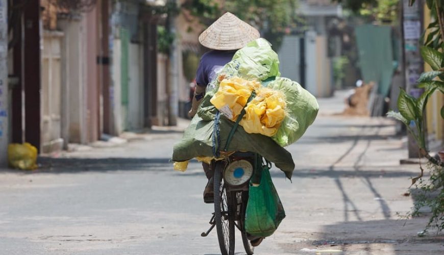 Mujer en bicicleta portando muchas cosas con ella. Viajar a Vietnam.